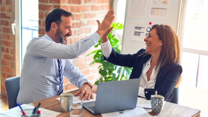 Mann und Frau im Büro vor Rechner geben sich High-Five